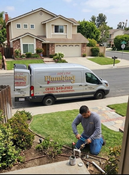 Hotline Plumbing technician working on outdoor plumbing repair at residential home